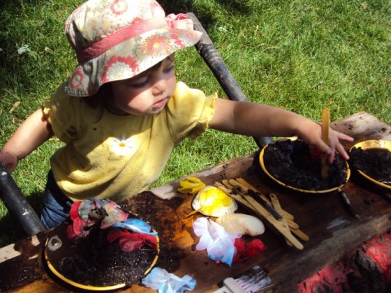 toddler making mud pies in wheelbarrow