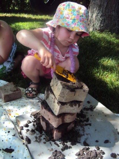 preschooler stacking bricks troweled with mud