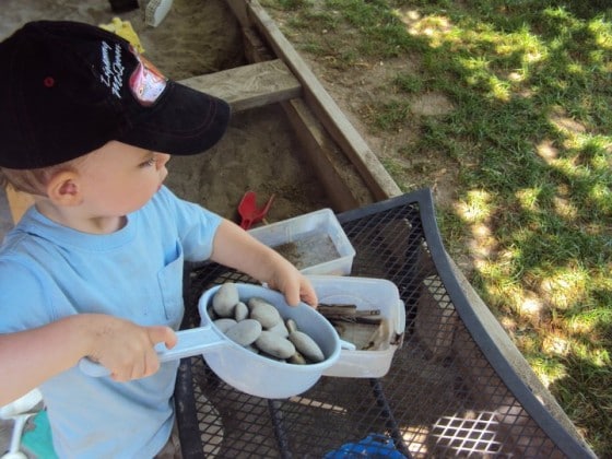 toddler playing with stones in sandbox