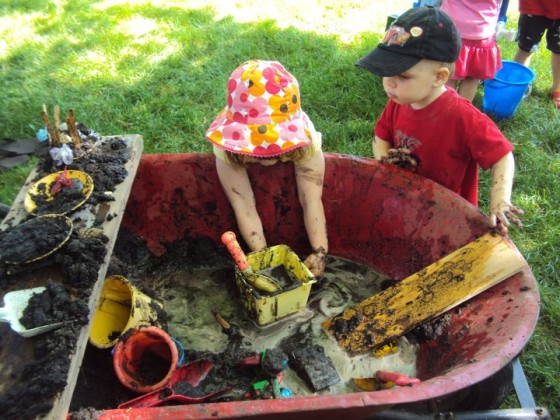 kids playing in wheelbarrow filled with mud