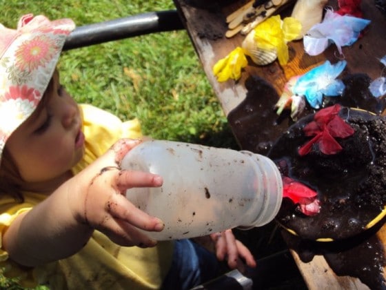 toddler pouring water on mud pie