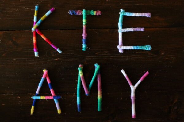 Yarn wrapped twig letters on dark wood table
