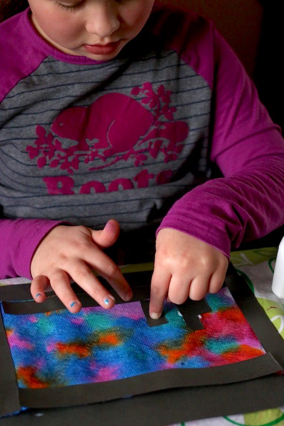 9 year old making gluing black paper to coloured paper towels