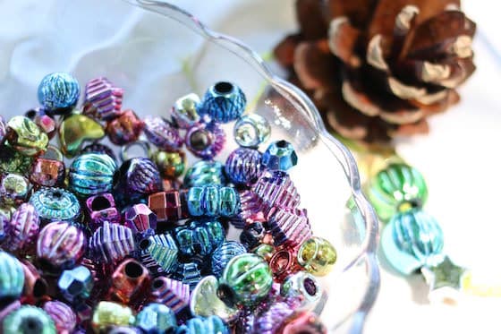 bowl of metallic beads beside pinecone