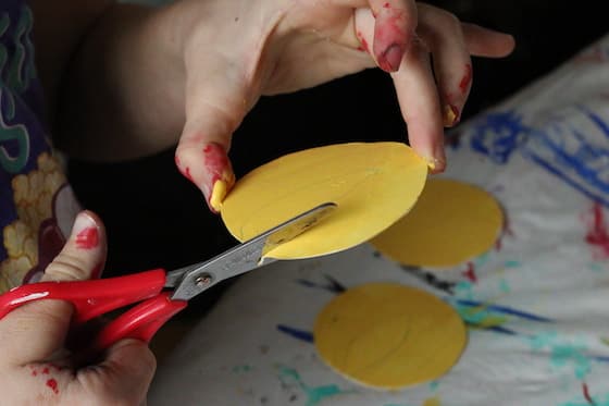 child's hands cutting yellow paper flame with red scissors