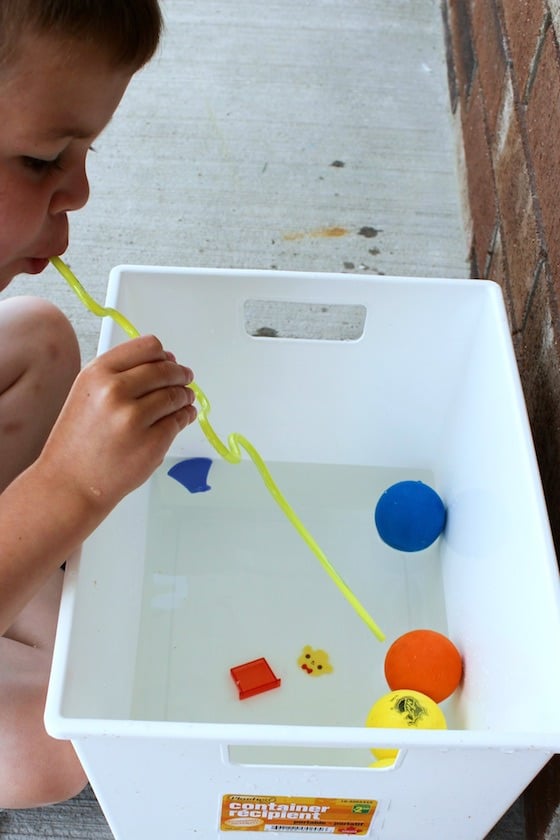 child blowing through straw to move toys on water