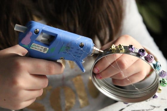 child gluing beads to mason jar lid