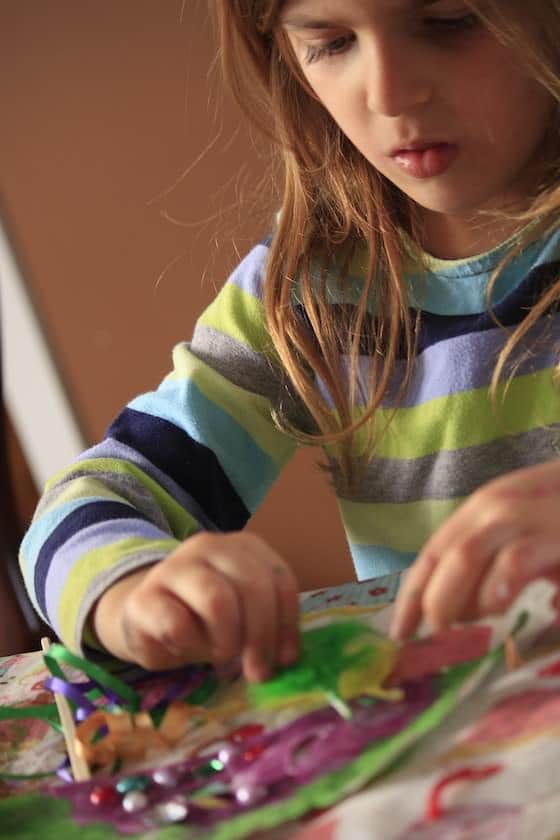 Child gluing green and yellow feathers to mask