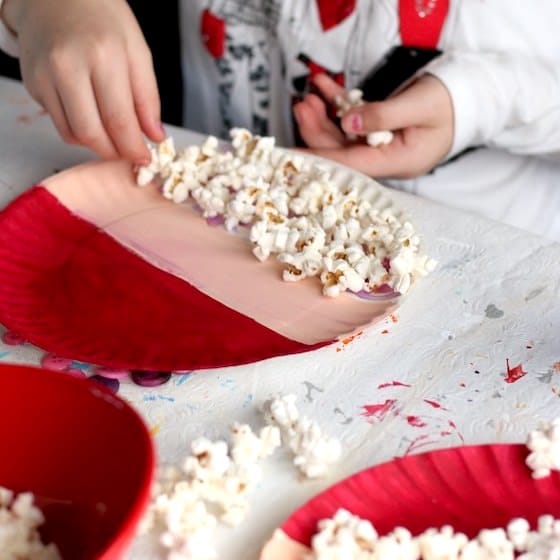 child gluing popcorn beard on paper plate santa