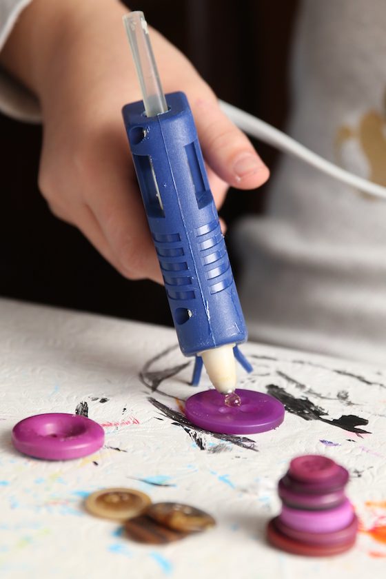 Child gluing purple buttons together with glue gun