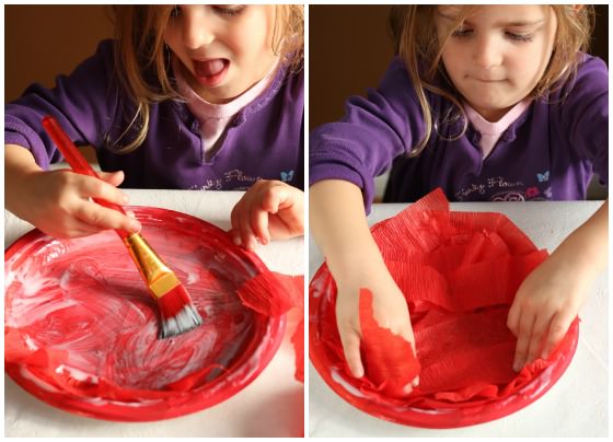 child gluing red crepe paper to painted paper plate