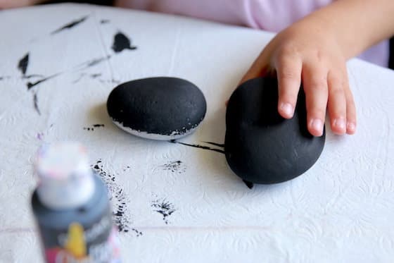 Child painting beach stone with black acrylic paint