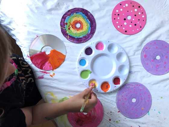 Child painting CDs with paints in paint pallet