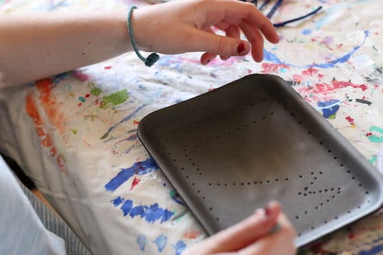 Child poking holes in styrofoam tray with pencil