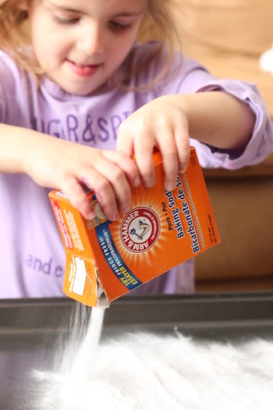 child pouring baking soda on baking sheet