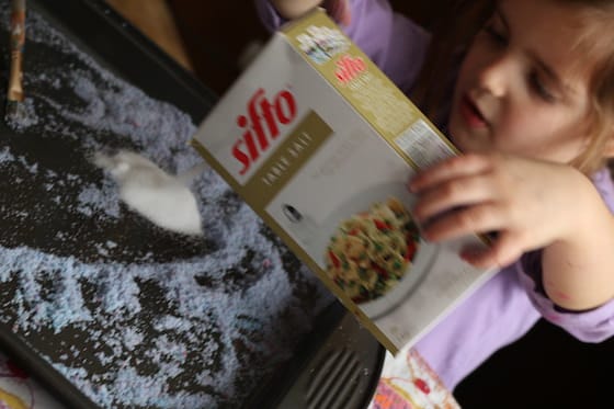 child pouring salt on a baking sheet.