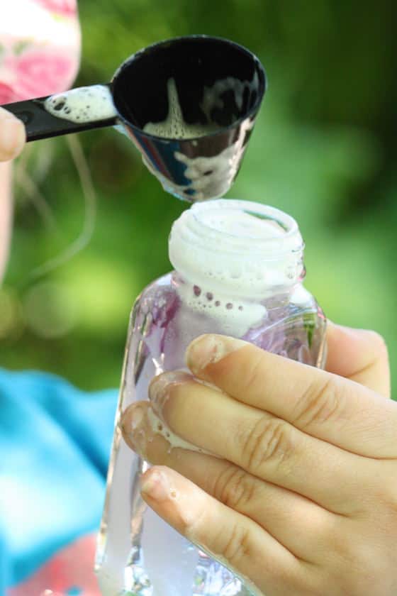 child stirring soapy water in glass bottle