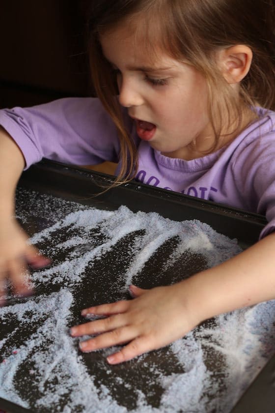 child swishing hands in a baking sheet filled with salt