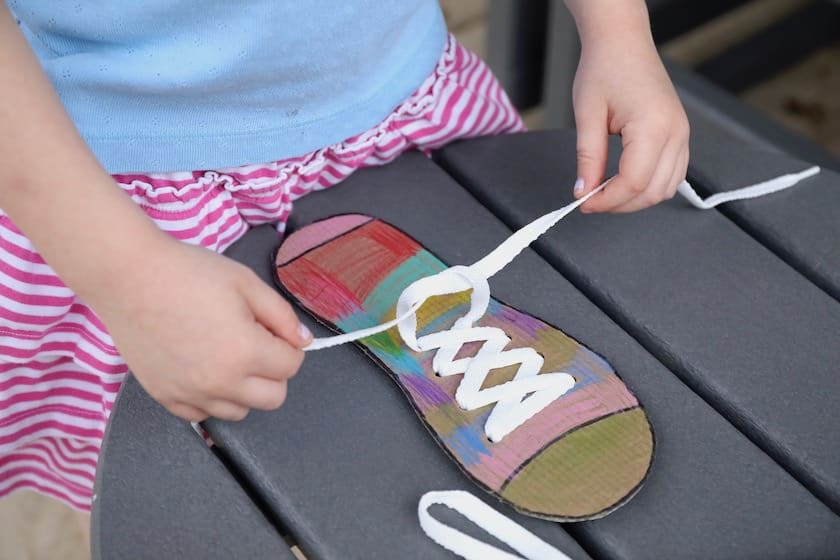 child tying shoelace on cardboard shoe