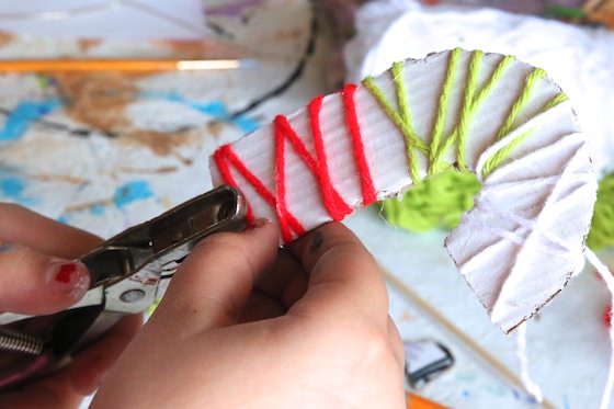 child wrapping cardboard initial with red, green and white yarn