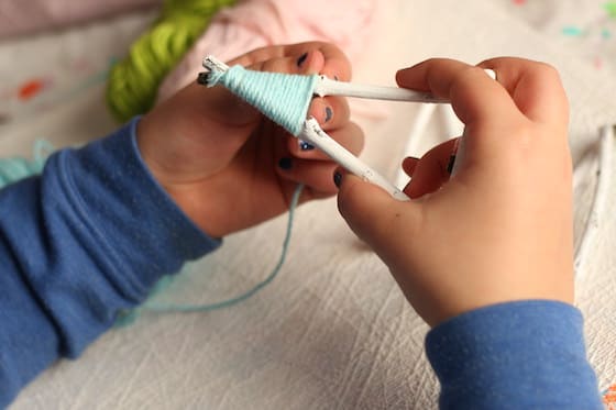 child wrapping twig tree with yarn