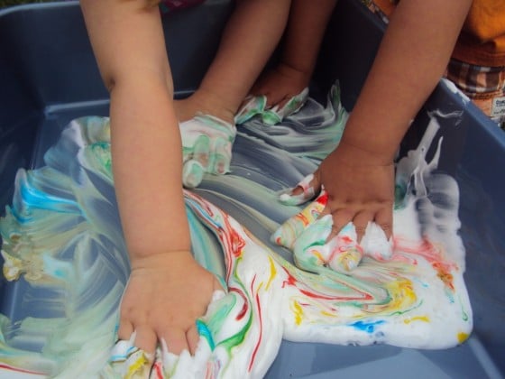 kids mixing food colouring into bin of shaving cream