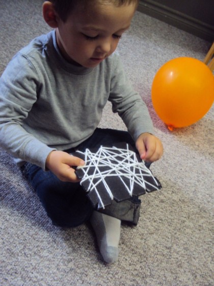 Toddler weaving yarn around a styrofoam produce tray