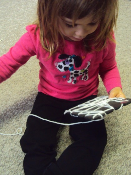 toddler weaving a spiders web with yarn