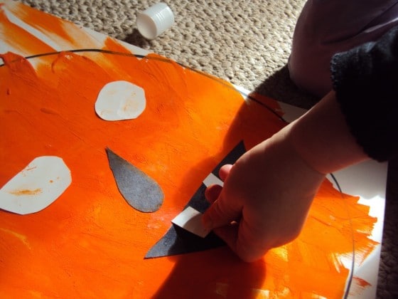 Preschooler gluing paper teeth on painted jack-o-lantern face