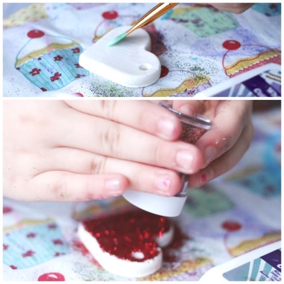 child gluing red glitter on white heart homemade clay ornament 