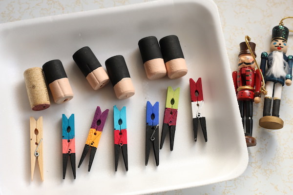 store-bought nutcracker ornaments beside tray of painted clothespins and corks 