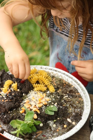 child decorating a mud pie with dried pasta and lentils