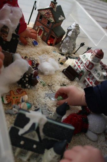 preschoolers playing in Christmas sensory bin of rice and village houses and people