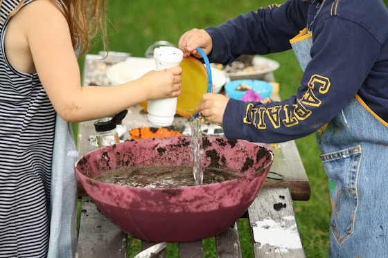 preschoolers adding water to bowl of mud in the mud kitchen