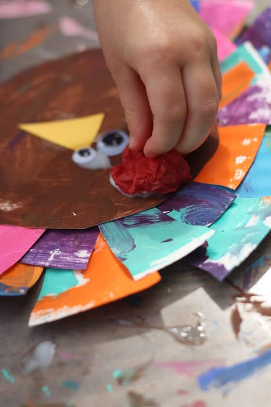 child gluing red tissue paper comb on turkey