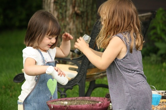 preschoolers shaking sand into bowl of mud 