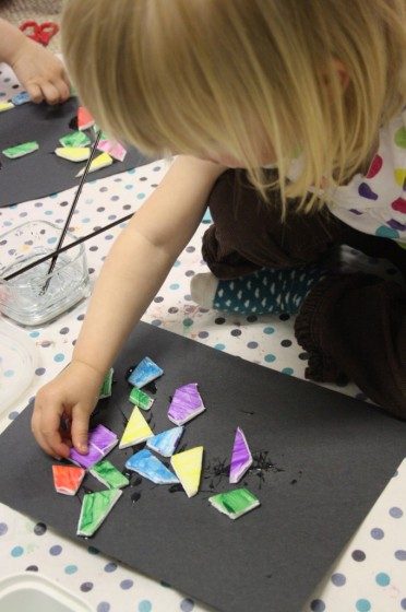 toddler gluing painted styrofoam pieces into mosaic art