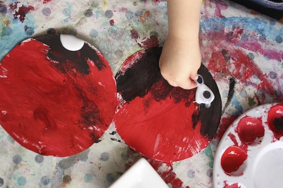 adding black paint and googly eyes to red paper plate