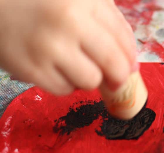 preschooler stamping black paint on red paper plate poppy