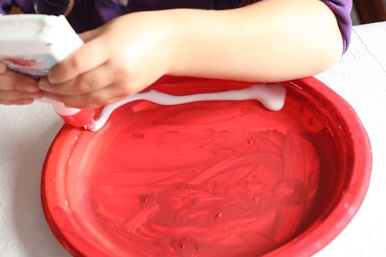 preschooler squeezing glue on red paper plate