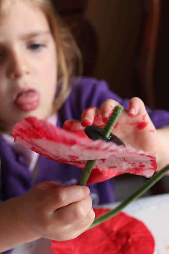 preschooler putting pipe cleaner stem and black button on poppy craft