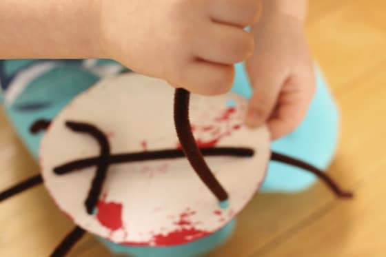 threading pipe cleaner "legs" through holes punched in paper plate