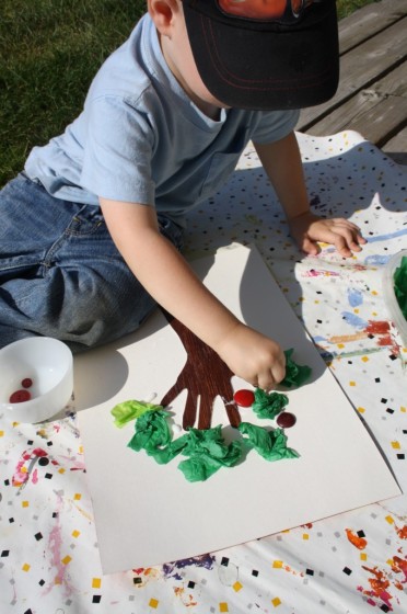 little boy gluing red buttons for apples