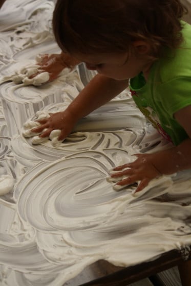 preschoolers swirling shaving cream on a table with their hands