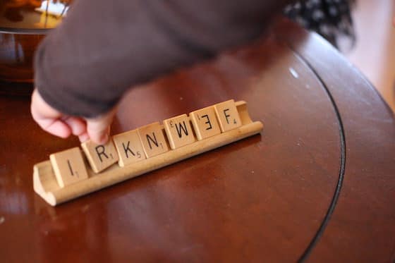 child placing scrabble tiles on wooden scrabble tray