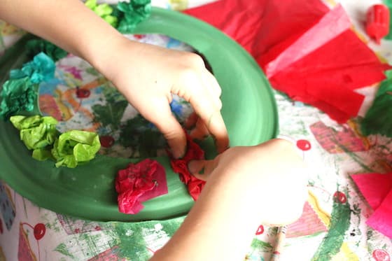 child gluing tissue paper to painted paper plate