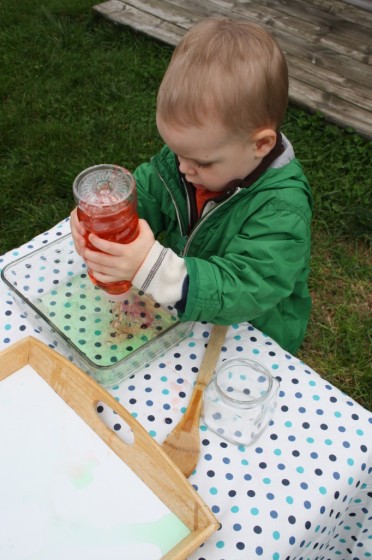 toddler squirting red water into baking dish