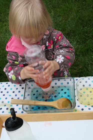 toddler squirting red water into blue water