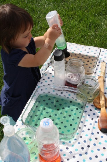 toddler squirting green water into glass dish 