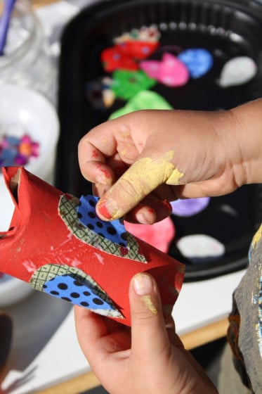 child gluing fabric wing on red toilet paper roll owl